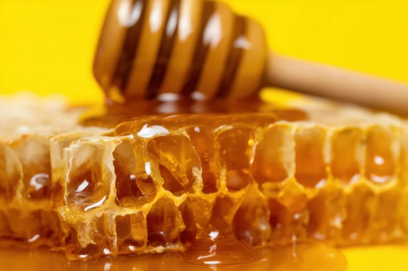 Honeycomb with dripping honey and wooden dipper on yellow background