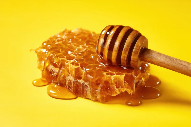 Honeycomb with dripping honey and wooden dipper on yellow background