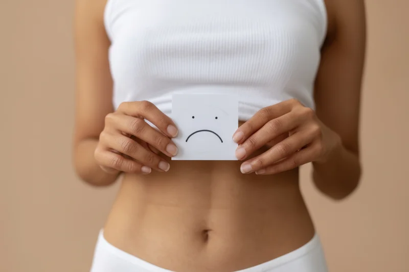 Woman holding sad emoticon card over her stomach