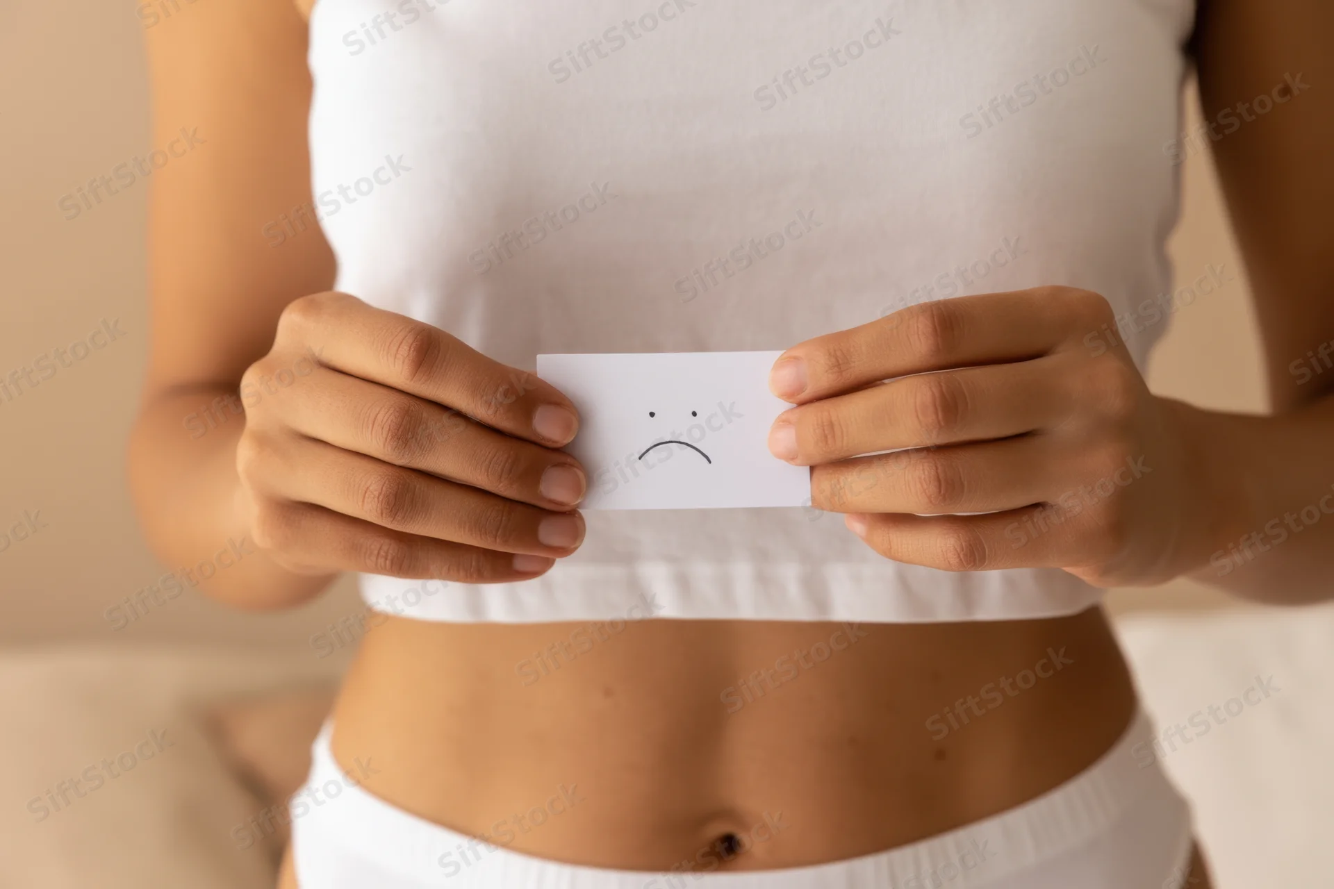 Woman holding small white card with hand-drawn sad emoticon in front of her midriff