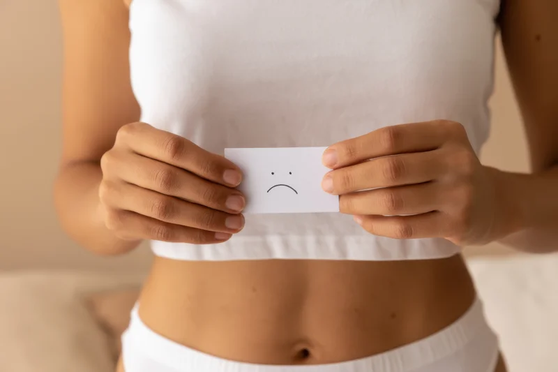 Woman holding small white card with hand-drawn sad emoticon in front of her midriff
