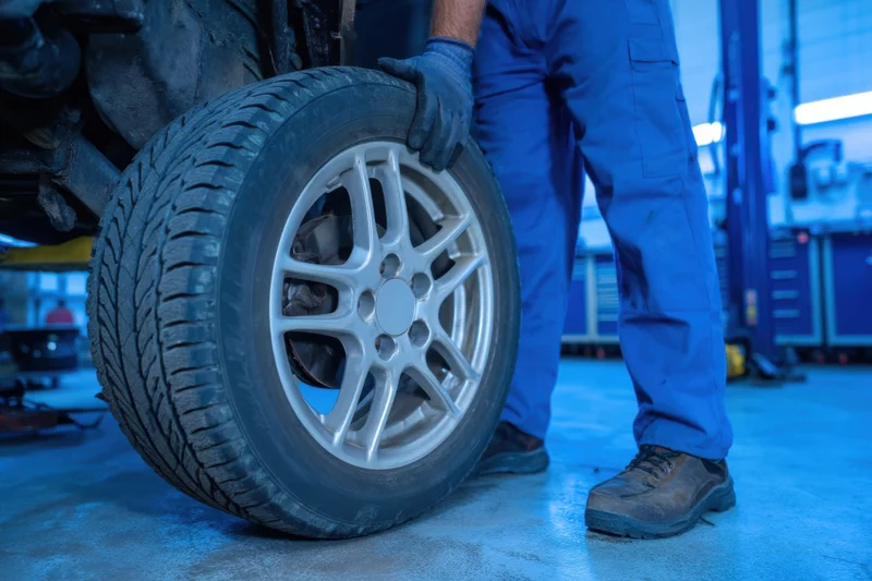 Mechanic holding car tire with alloy rim in garage workshop