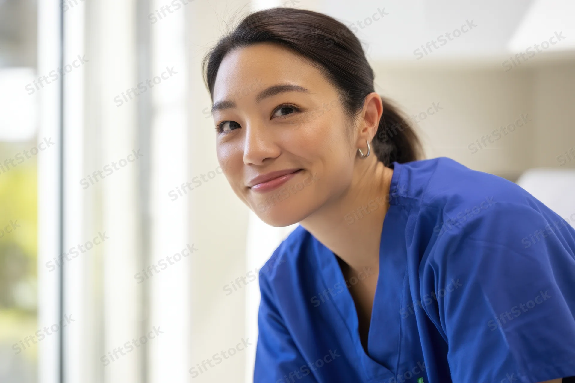 Smiling female healthcare professional in blue scrubs indoors near window