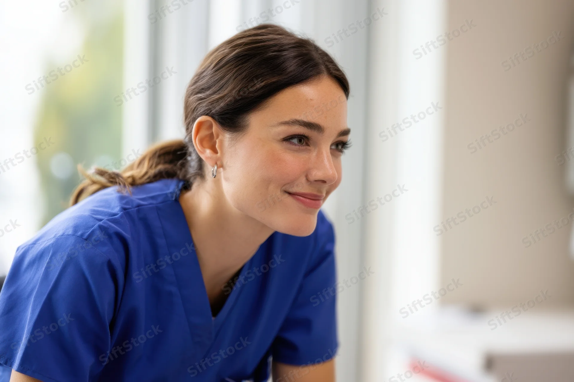 Nurse in blue scrubs smiling while looking to the side in a clinic setting