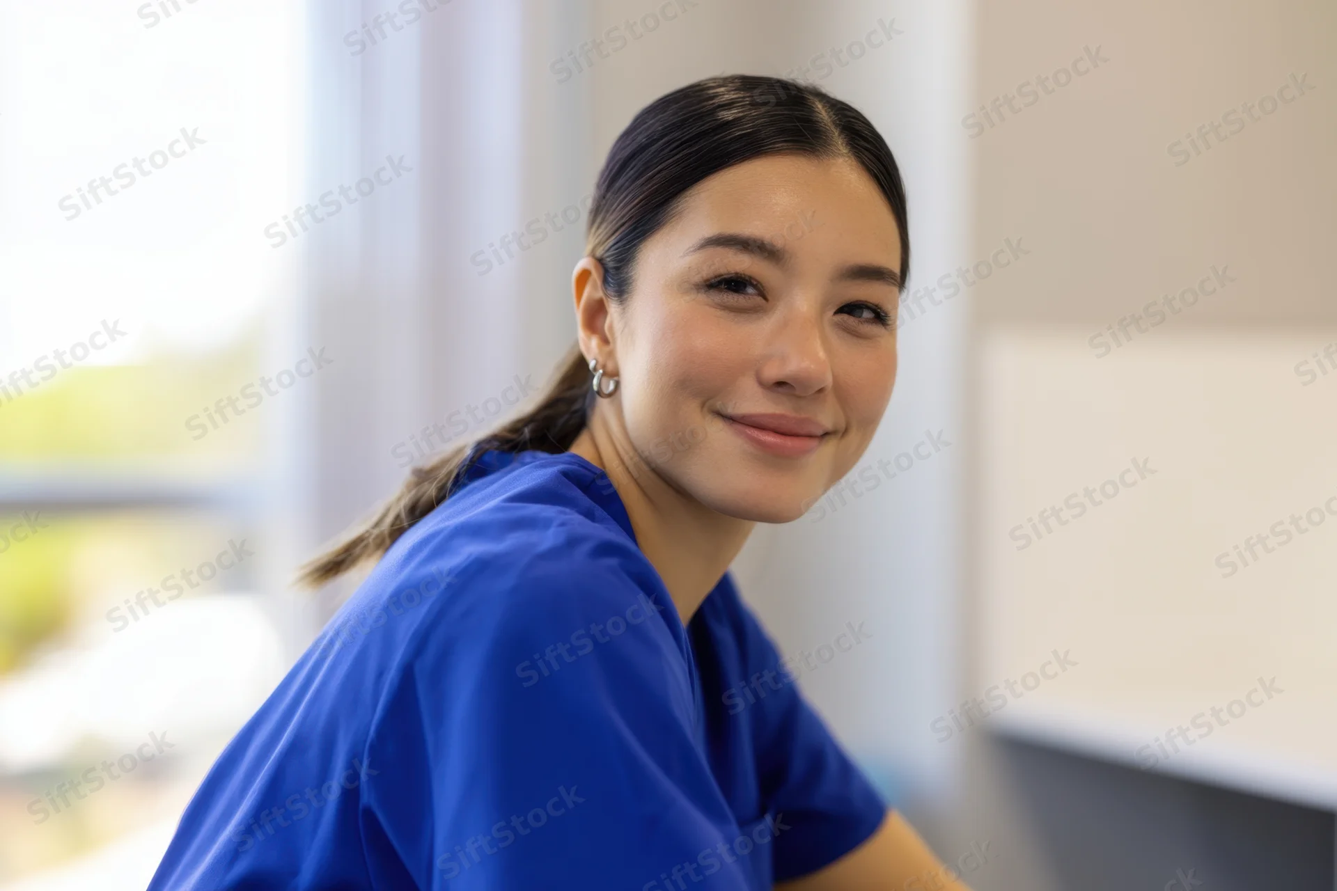 Woman in blue scrubs smiling while turning head in a medical office setting