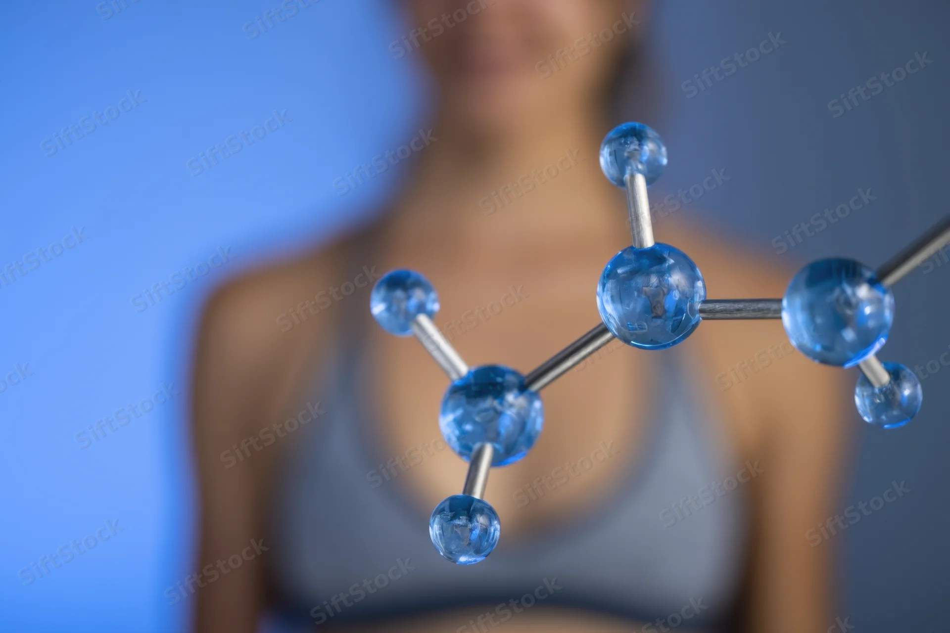 Molecular model in blue glass spheres connected by rods in front of a blurred woman's torso