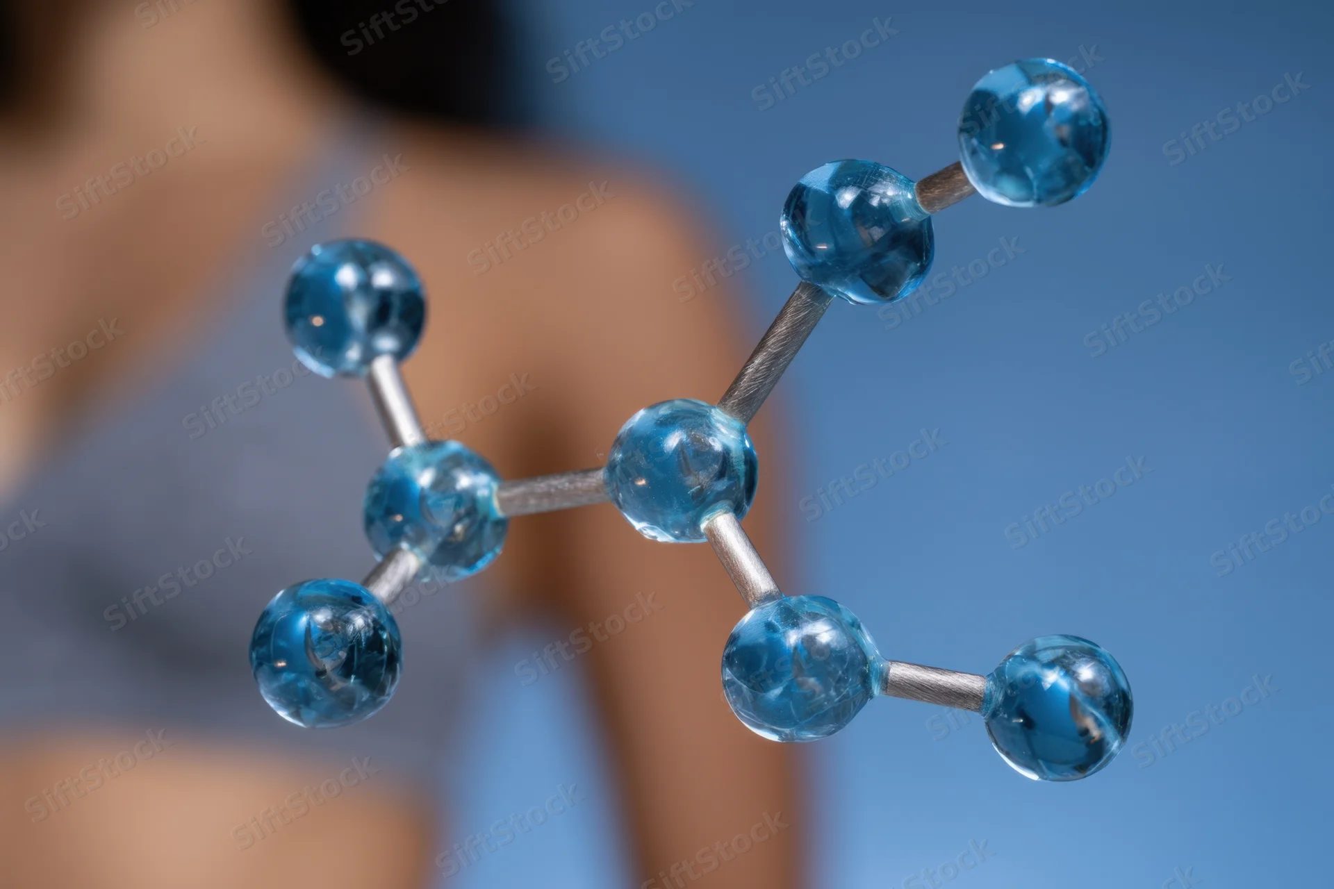 Molecular model with blue glass spheres connected by rods, shown in front of a blurred person in a lab setting