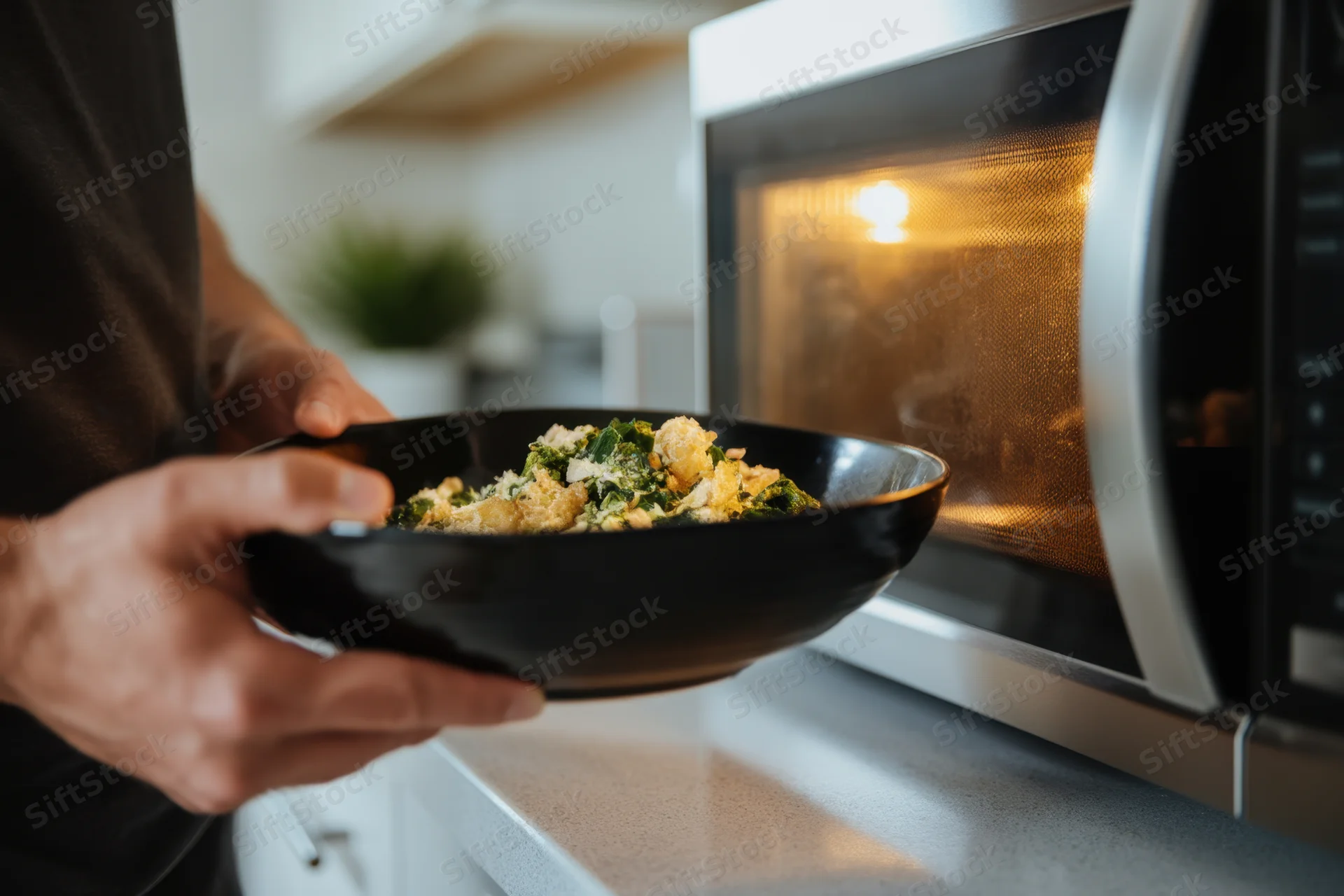 Man holding bowl of food near microwave in kitchen