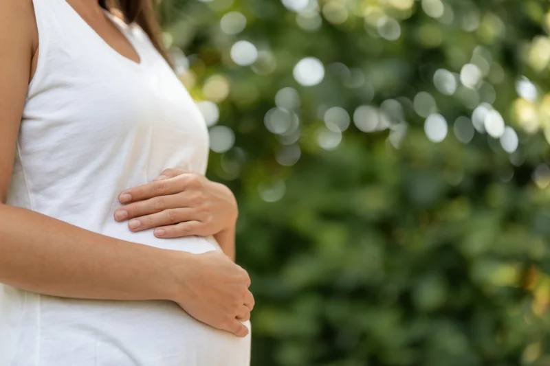 Pregnant woman cradling her belly outdoors in a green garden setting