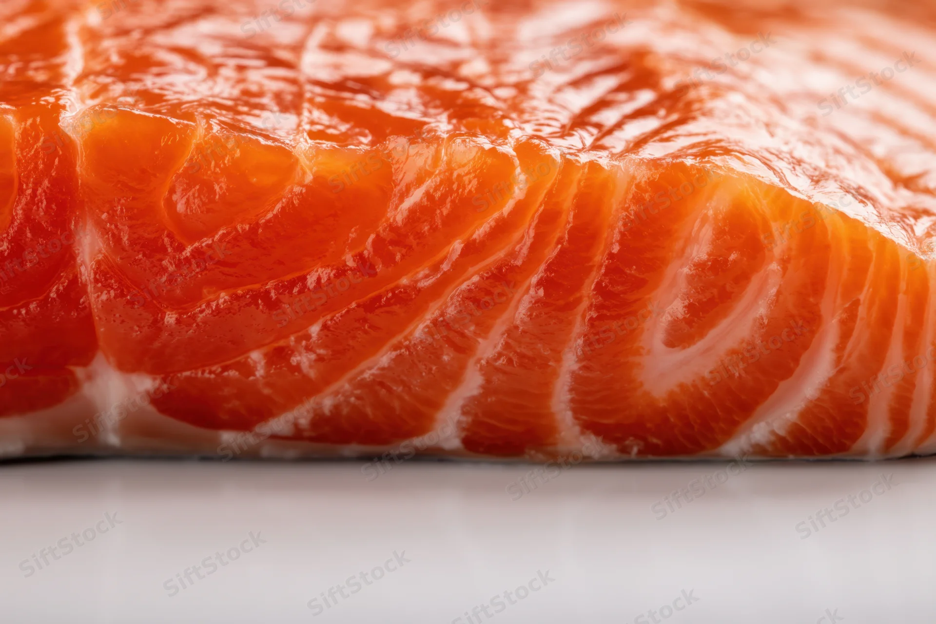 Macro close-up of a raw salmon fillet showing orange flesh and white fat striations on a plain surface