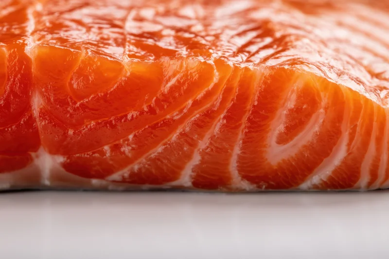 Macro close-up of a raw salmon fillet showing orange flesh and white fat striations on a plain surface
