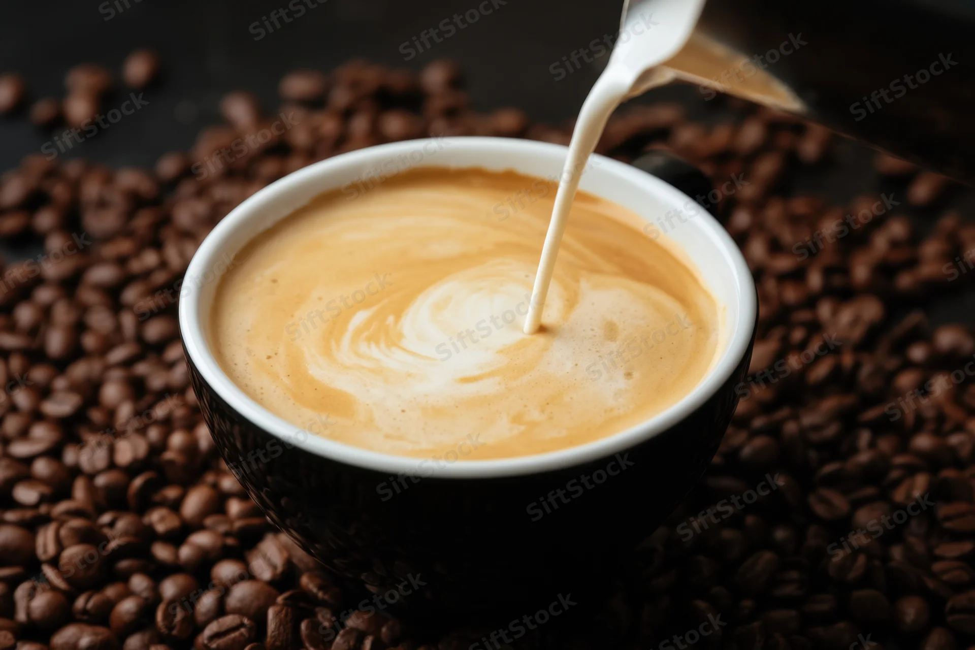Milk being poured into a black coffee cup with latte art forming on top surrounded by coffee beans
