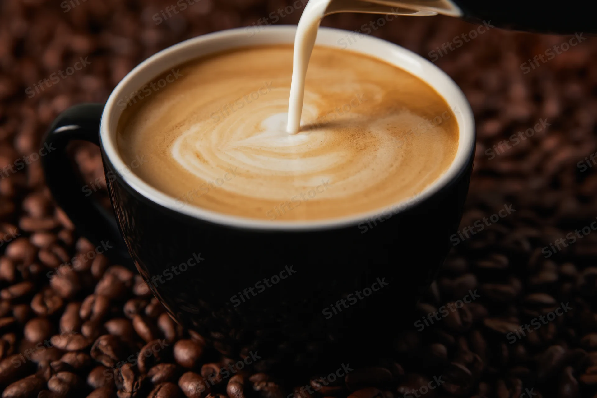 Milk being poured into a black coffee cup creating latte art on a bed of coffee beans