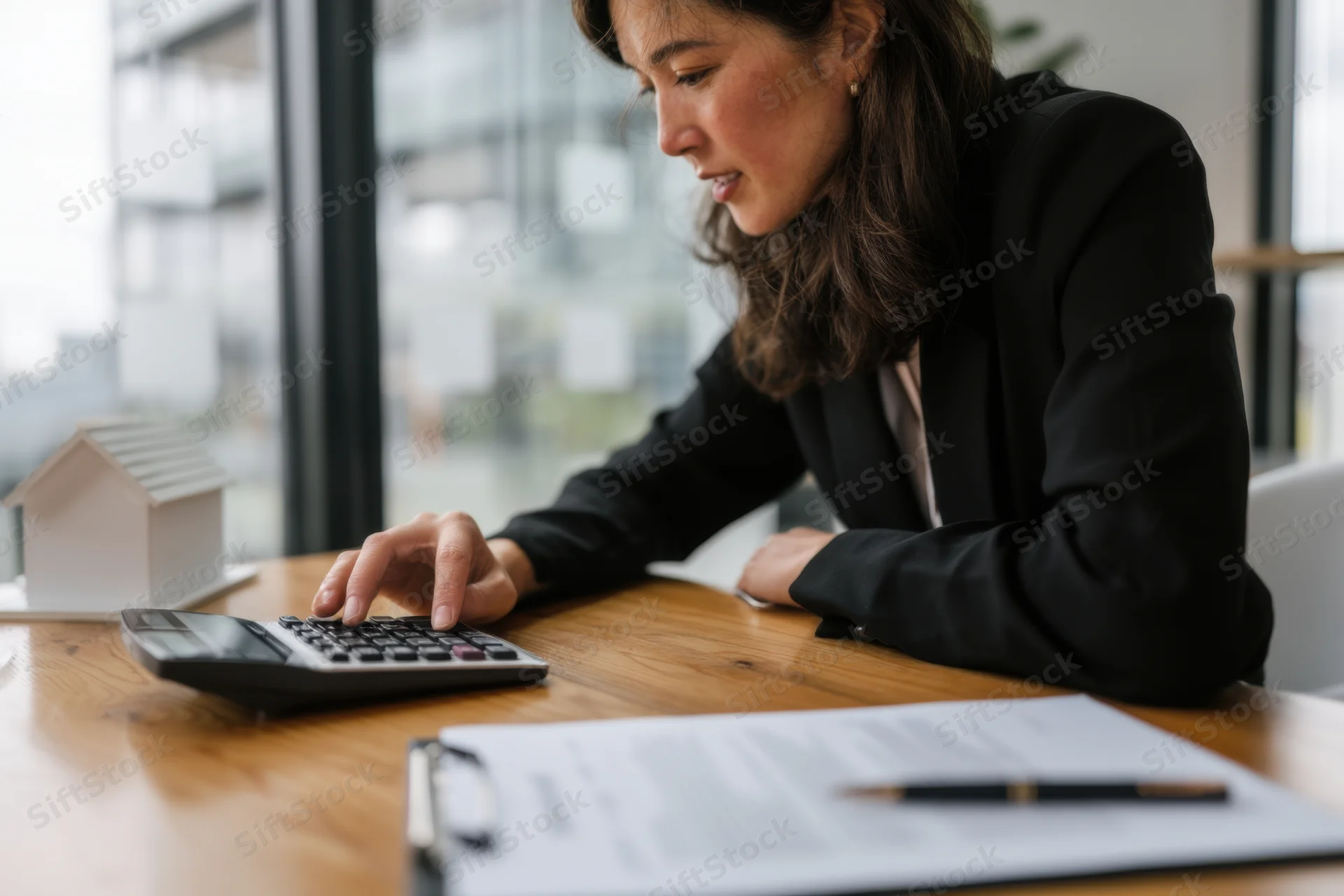 Woman in black blazer calculating on desk with calculator and home model in office
