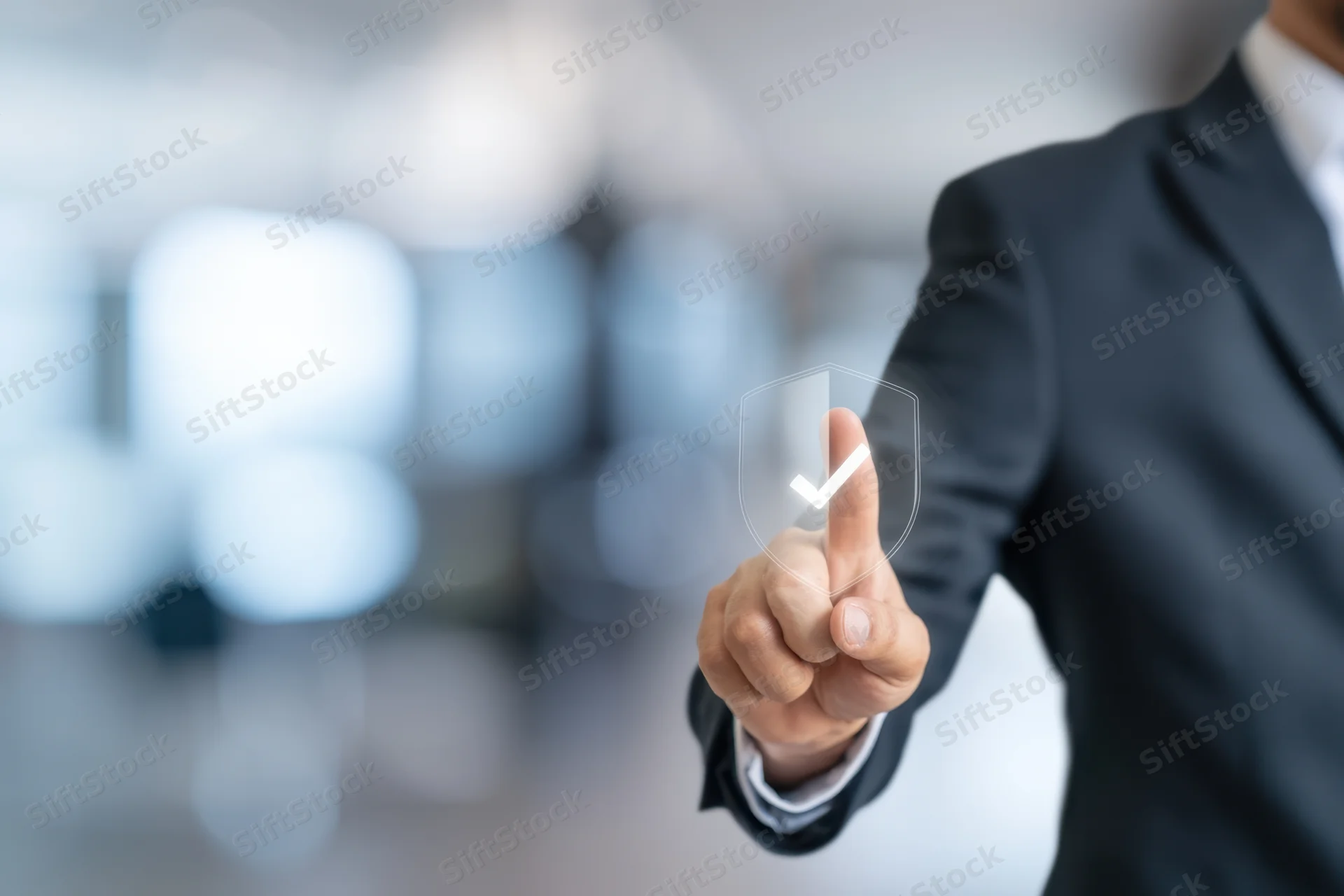 Businessman in dark suit pointing finger at transparent digital screen with shield and checkmark symbol in office setting