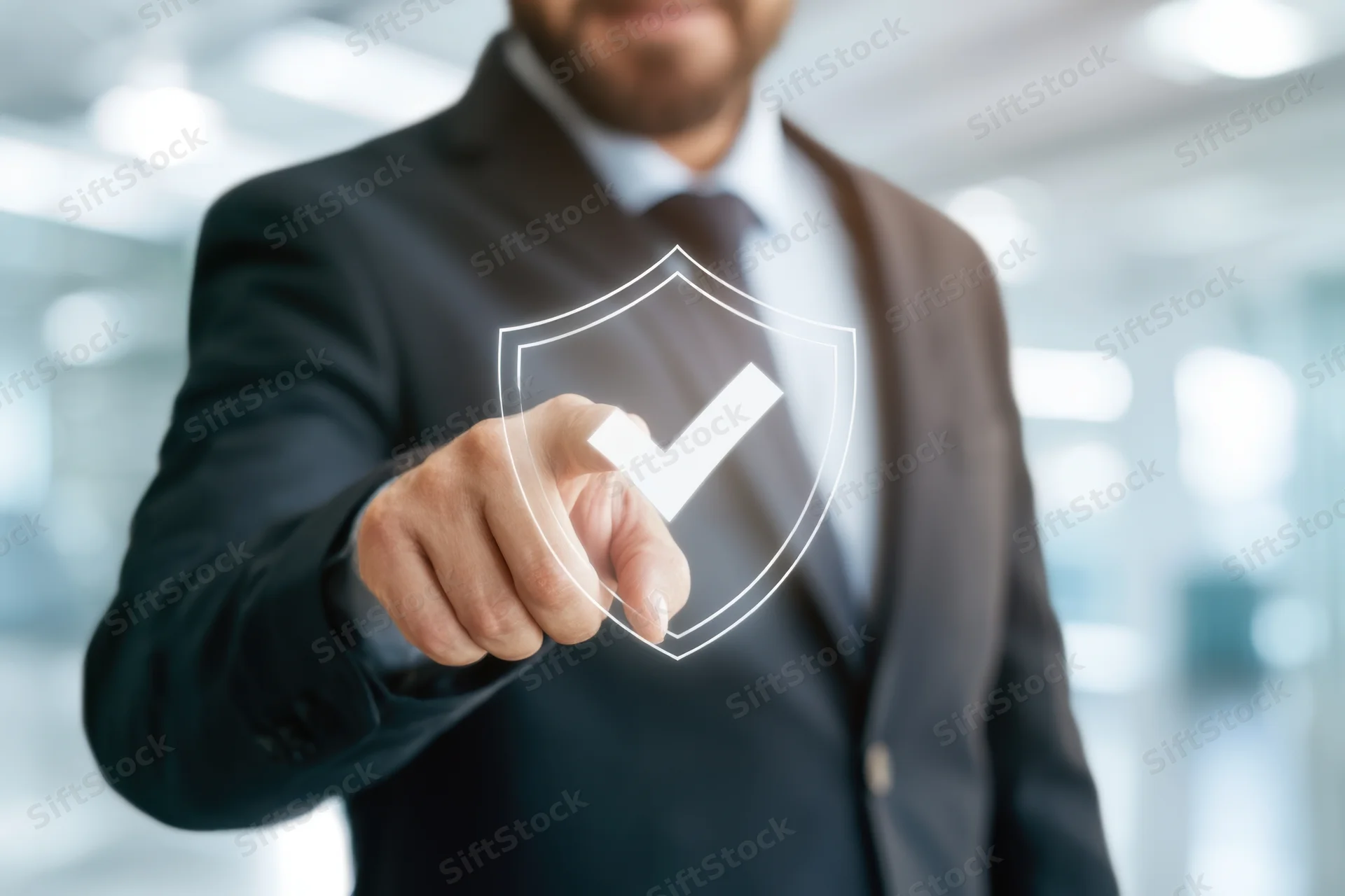 Businessman in dark suit pointing at transparent digital shield with checkmark in office interior