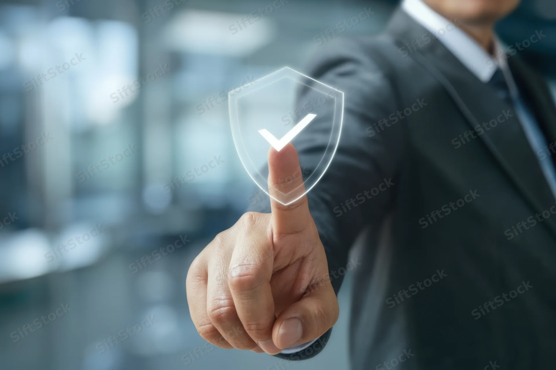 Businessman in dark suit pointing finger at transparent digital shield with checkmark in office setting