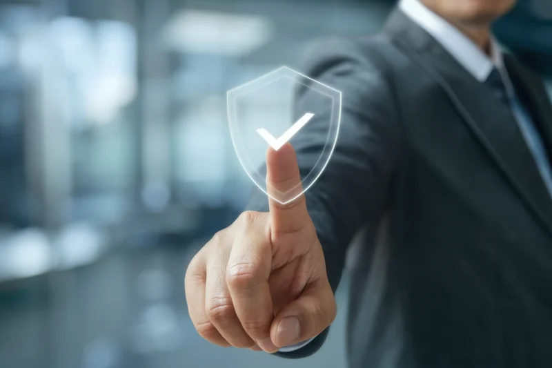 Businessman in dark suit pointing finger at transparent digital shield with checkmark in office setting