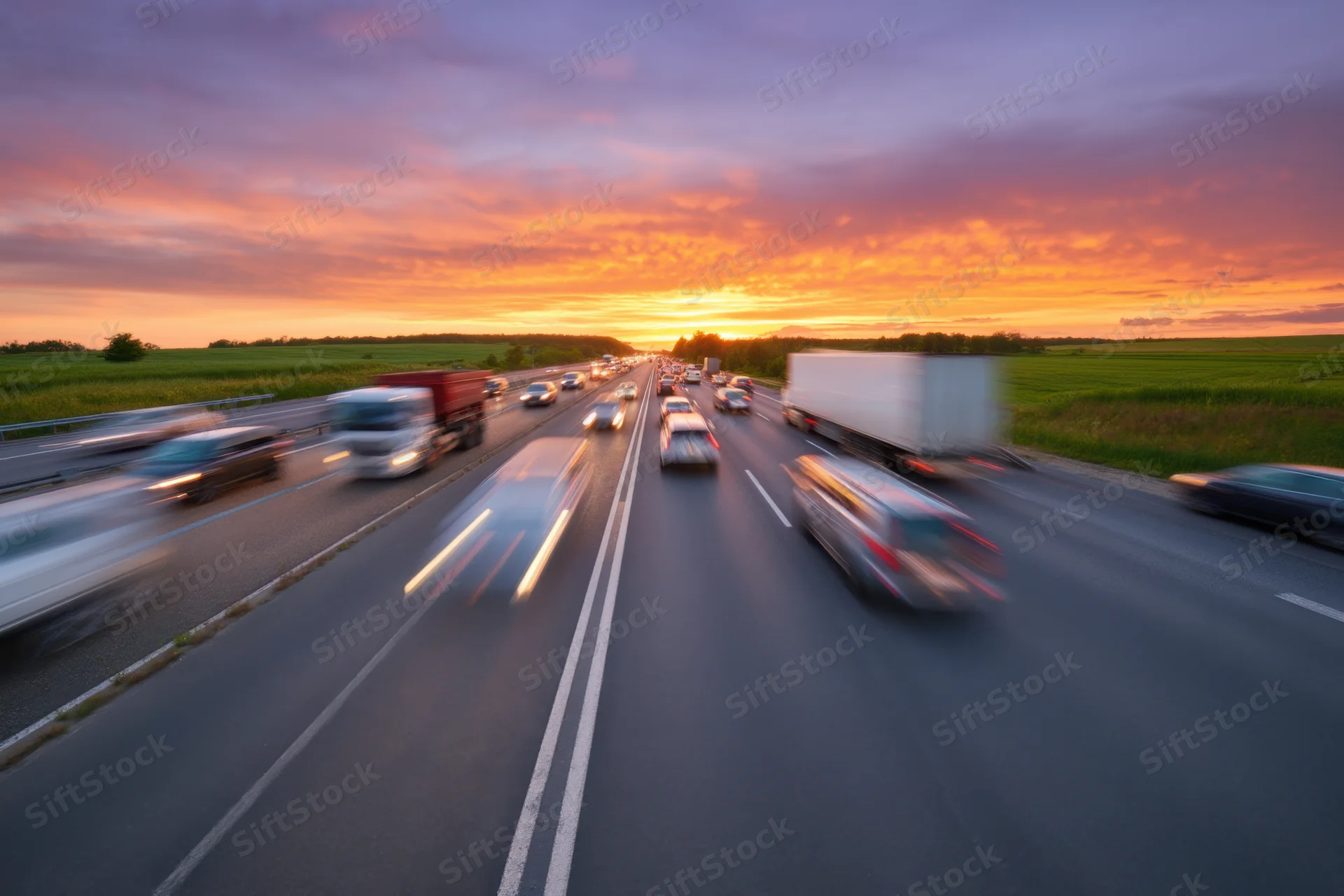 Busy highway with multiple lanes of moving vehicles during twilight sunset over rural fields