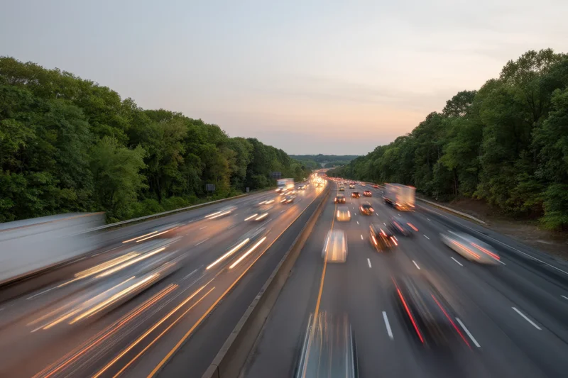 Motion-blurred vehicles moving on a multi-lane highway flanked by trees at dusk