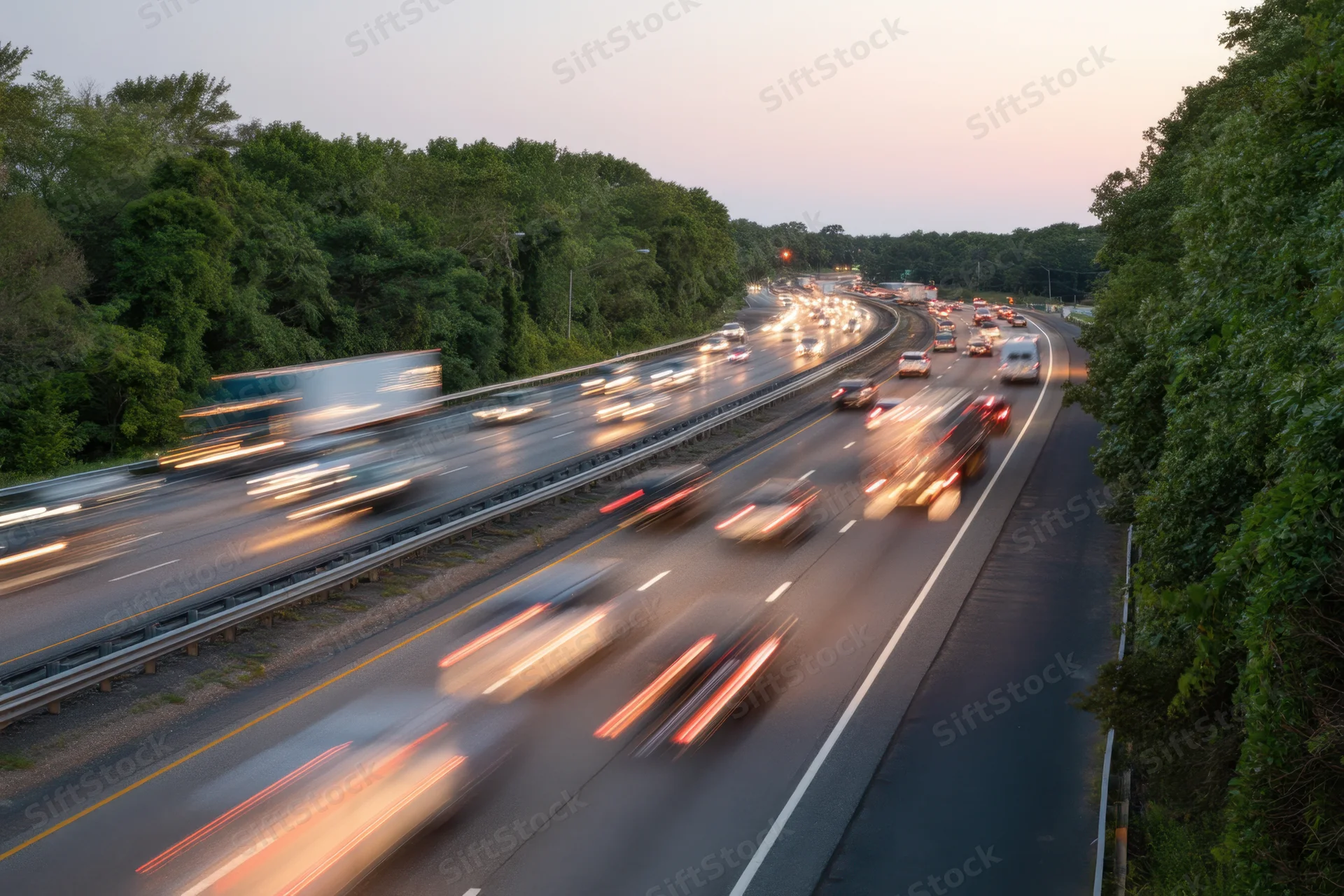 Busy highway with motion blur from moving vehicles during dusk surrounded by trees