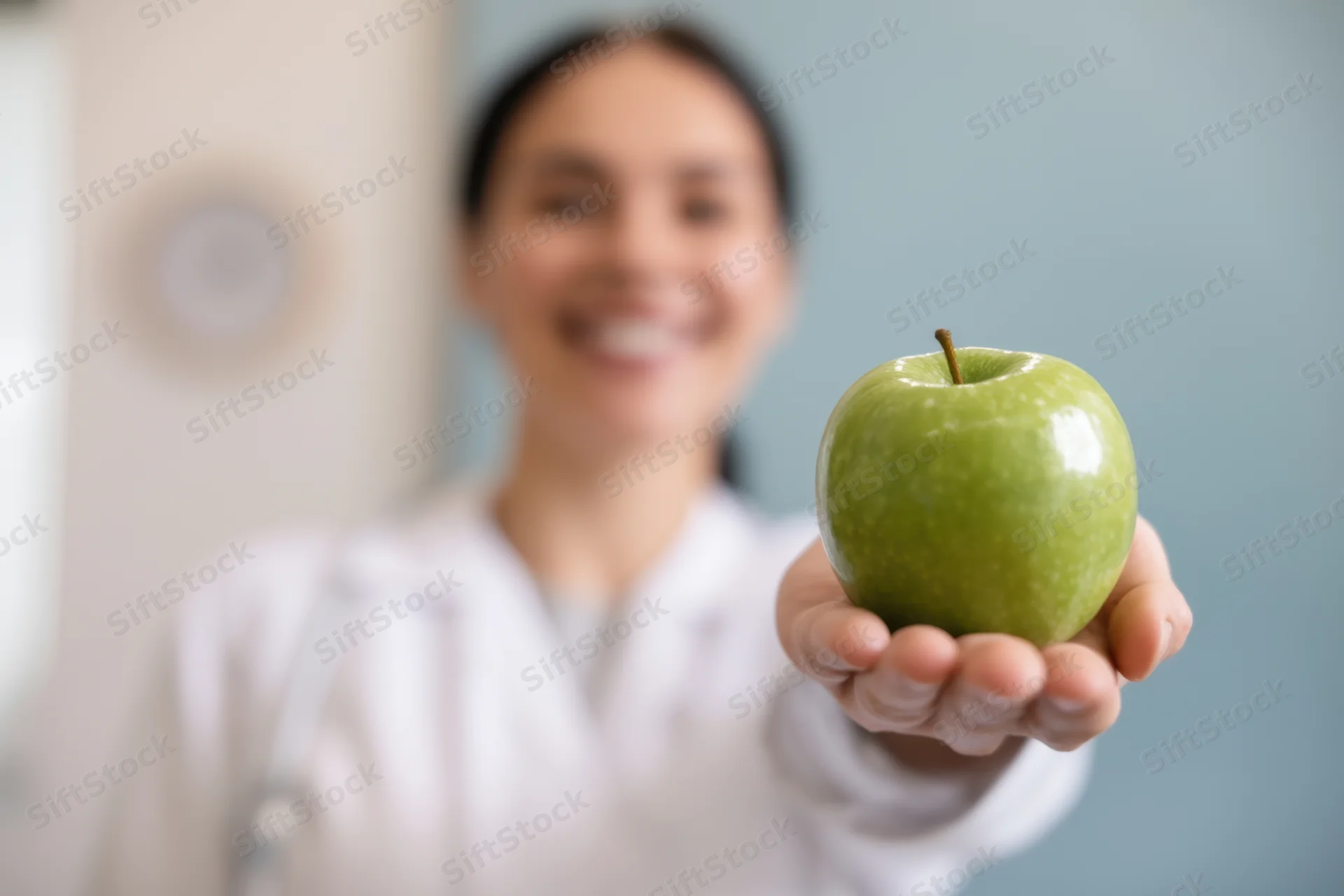 Woman in white coat holding green apple in clinic setting