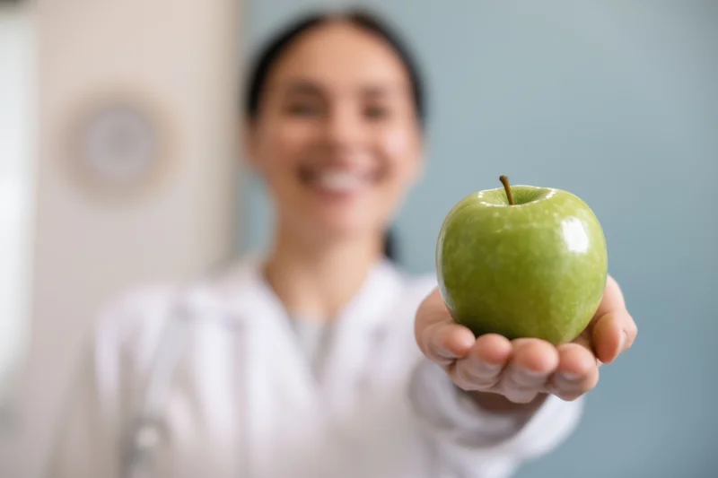 Woman in white coat holding green apple in clinic setting