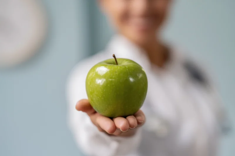 Woman in white coat holding green apple in hand, close-up focus on fruit with blurred background
