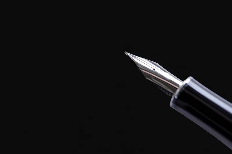 Close-up of a sleek metallic fountain pen nib against a black background