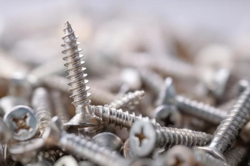 Closeup of metal screws piled together with one standing upright in focus