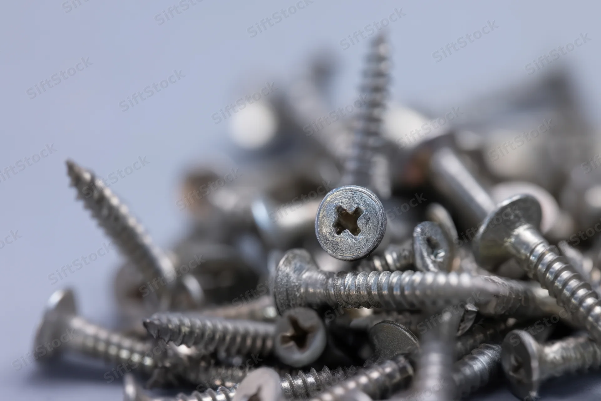 Close-up of a pile of metal screws scattered on a flat surface with shallow depth of field