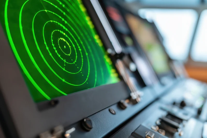 Close-up of a green radar display showing concentric circles and blips on a ship's bridge control panel