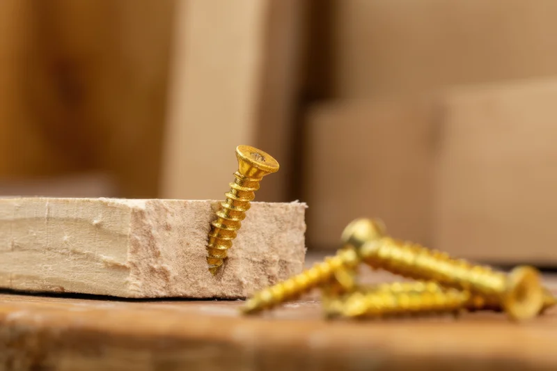 Golden screw embedded in a wooden plank with additional screws nearby on a workbench surface