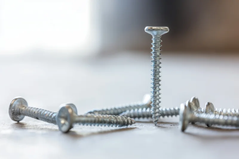 Silver screws scattered across a smooth surface with one standing upright, shallow depth of field