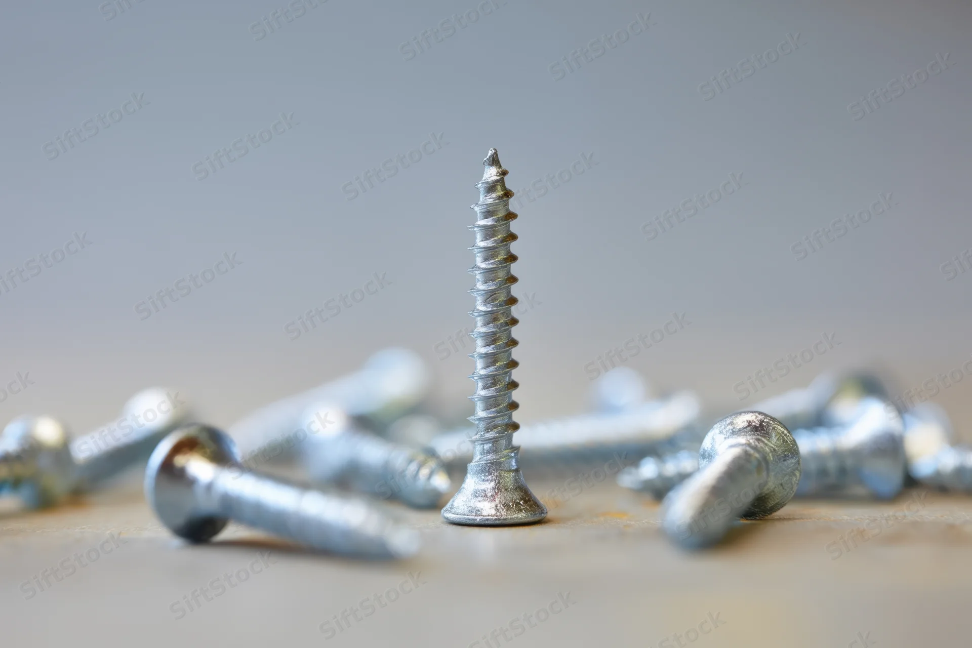 A single silver screw standing upright among scattered screws on a smooth surface