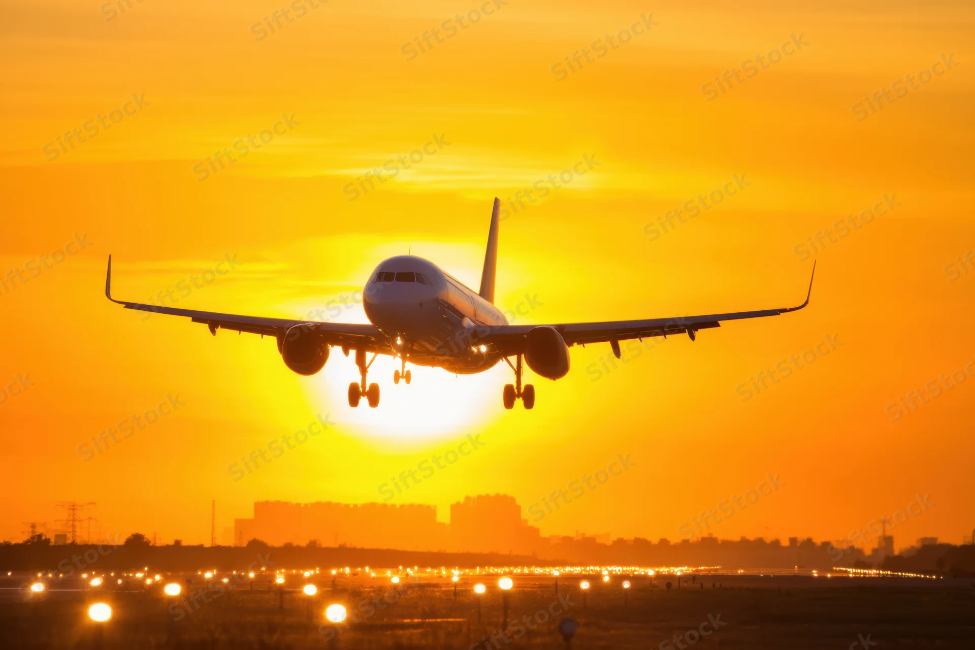 Commercial airplane landing on runway at sunset with city skyline in background