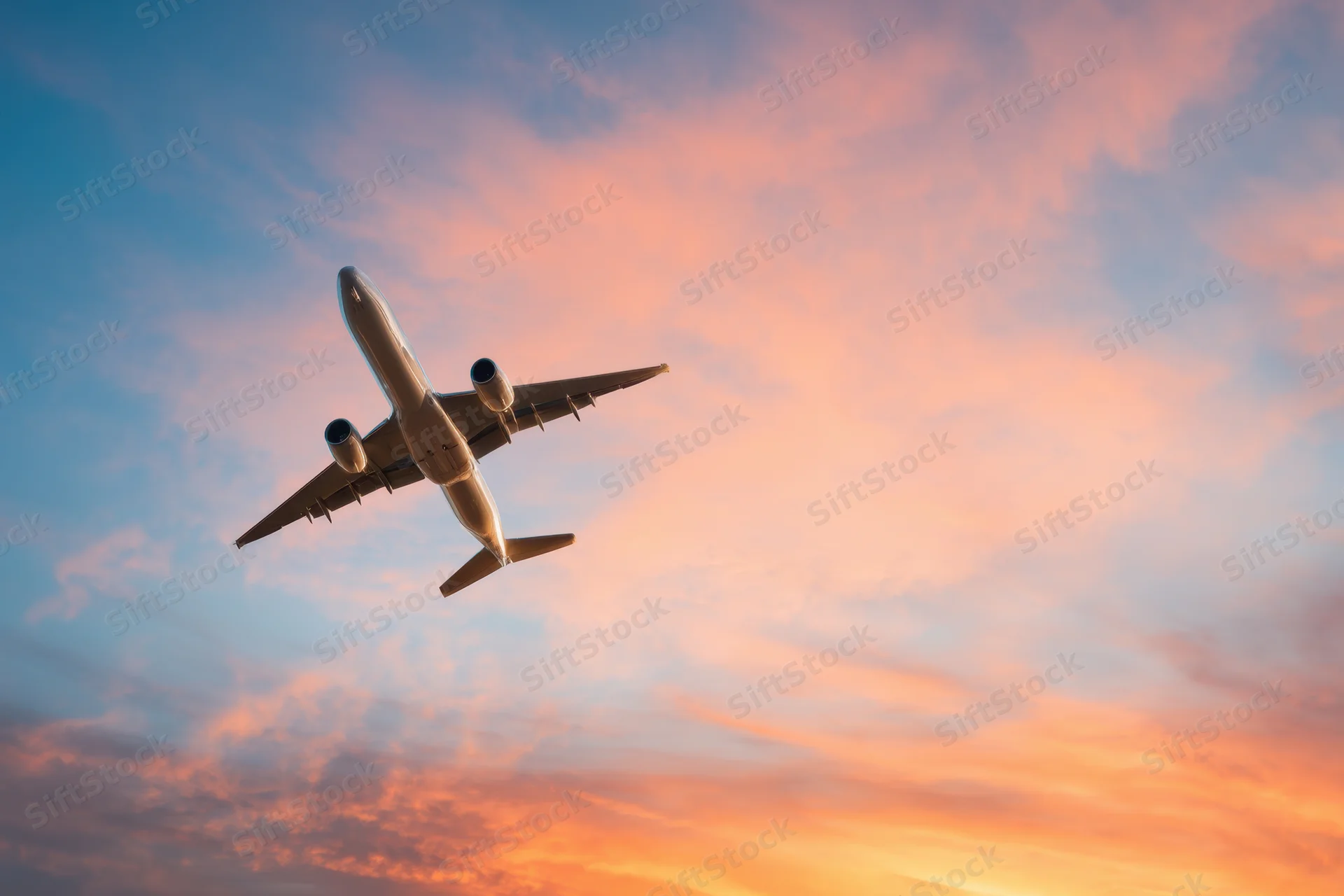 Commercial airplane ascending into sunset sky with pink and orange clouds