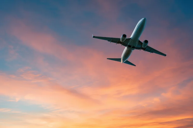 Commercial airplane ascending into twilight sky with orange and pink clouds
