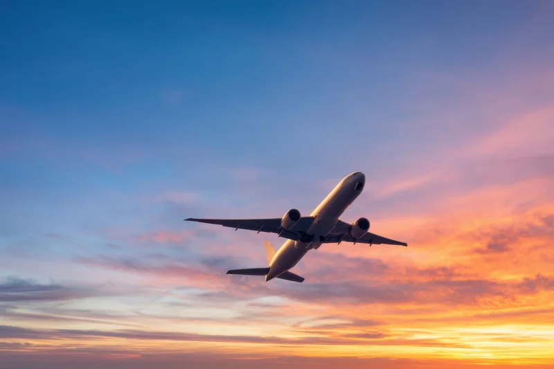 Commercial airplane ascending into twilight sky with colorful sunset horizon