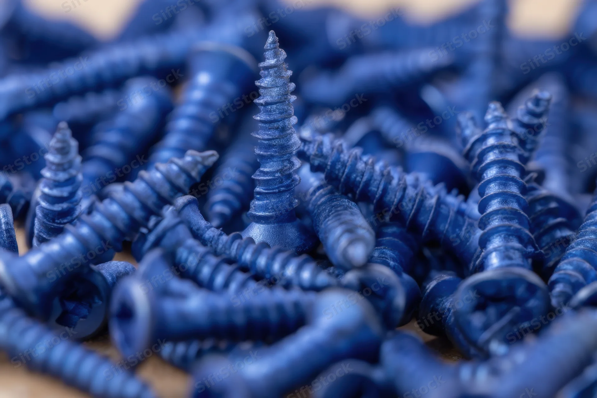 Dense arrangement of blue metallic screws with matte finish scattered on wooden surface