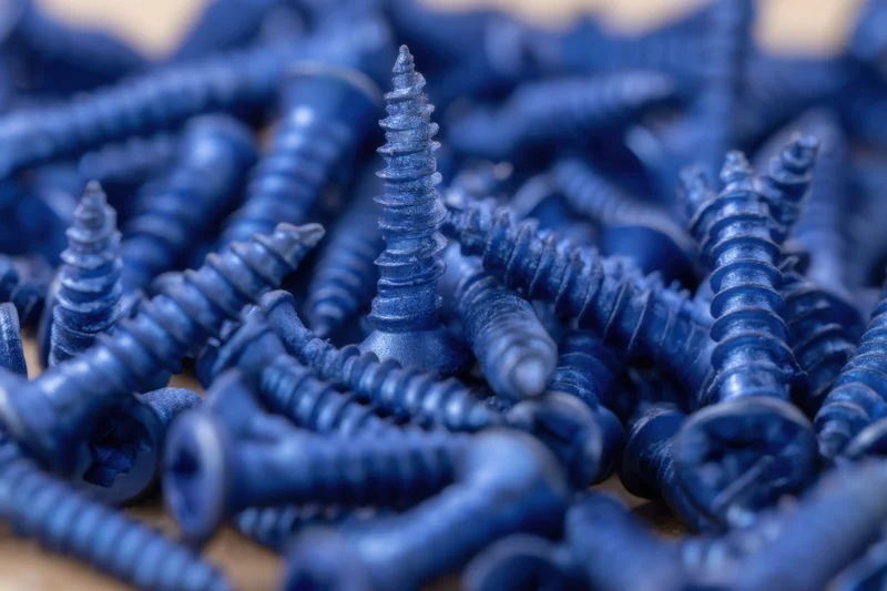 Dense arrangement of blue metallic screws with matte finish scattered on wooden surface