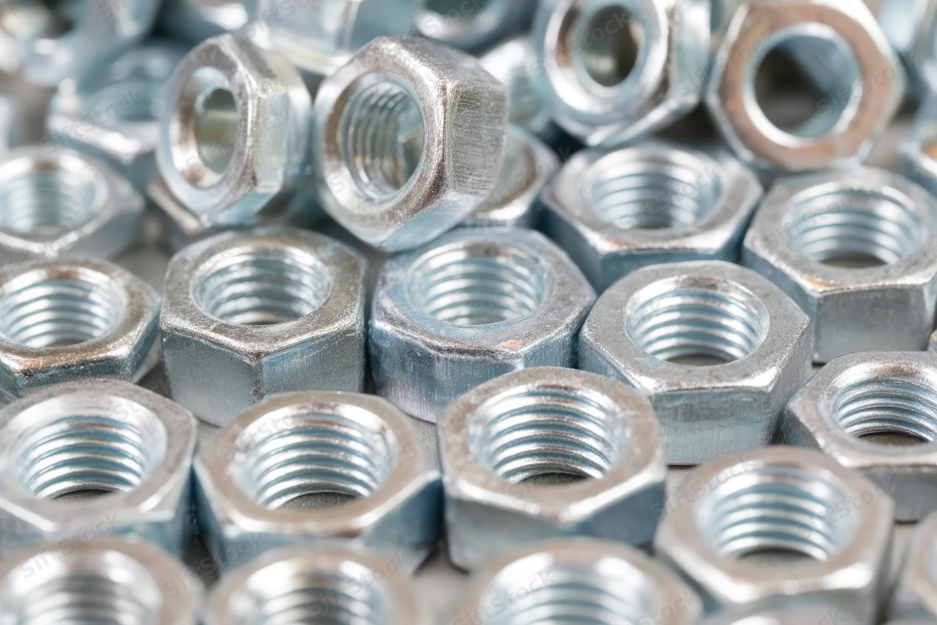 Closeup of metallic hex nuts and bolts densely arranged in a pile