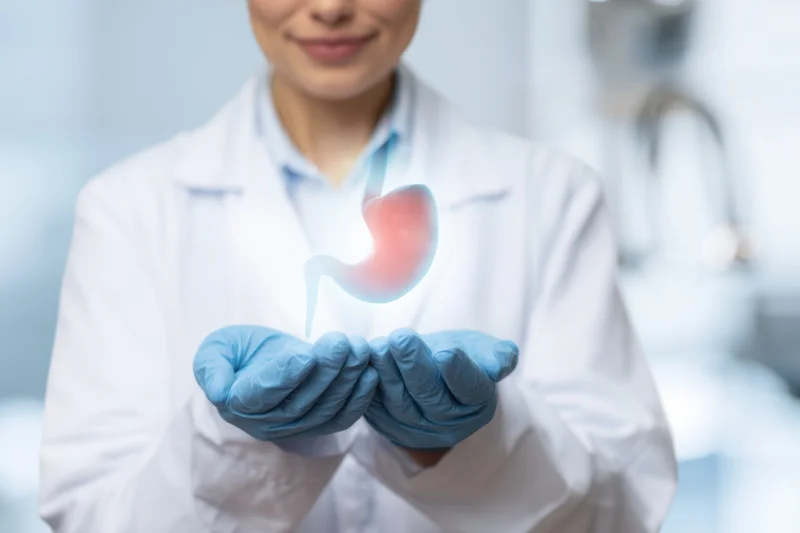 Woman doctor in lab coat holding holographic stomach model in gloved hands in clinical setting