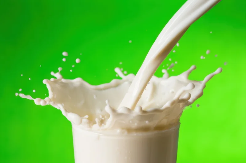 Milk pouring into a glass with dynamic splash and droplets against green background