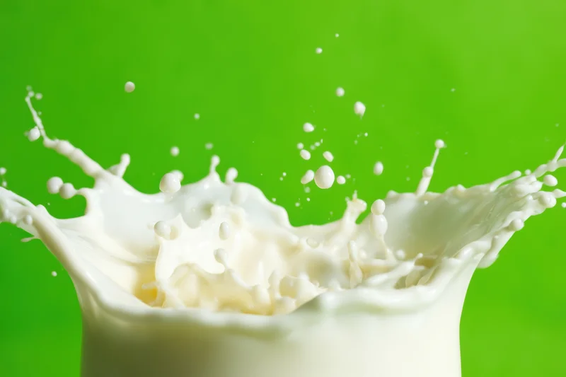 Dynamic splash of milk with droplets suspended in mid-air against green background