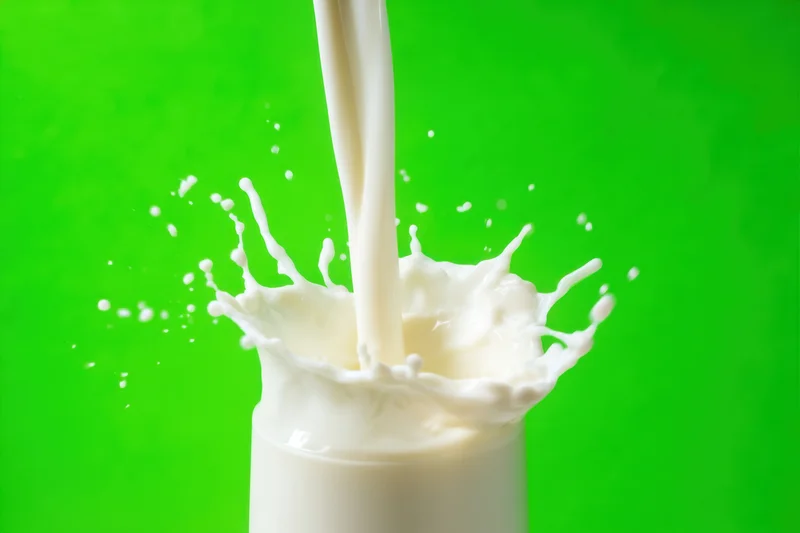 Milk pouring into a glass with dynamic splash and suspended droplets against green background
