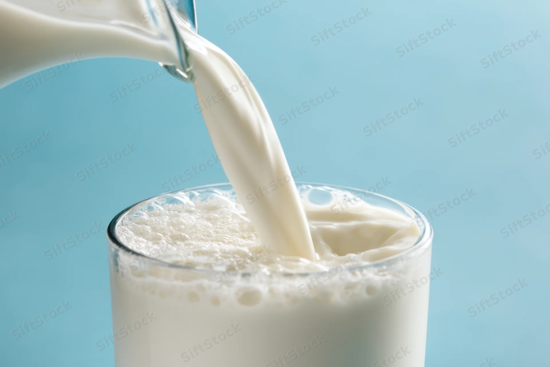 Milk being poured into a glass from a bottle against a blue background
