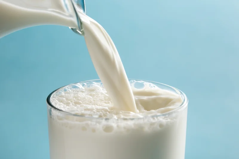 Milk being poured into a glass from a bottle against a blue background