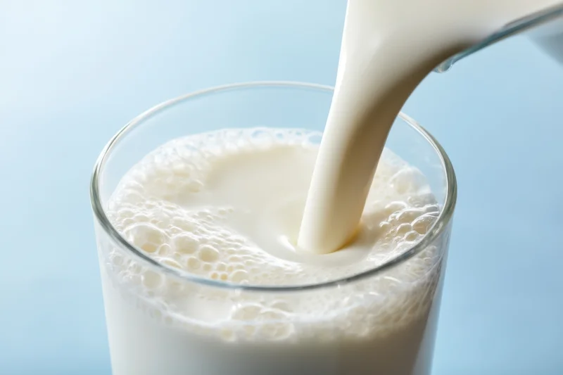 Milk being poured into a glass creating froth on a light blue background