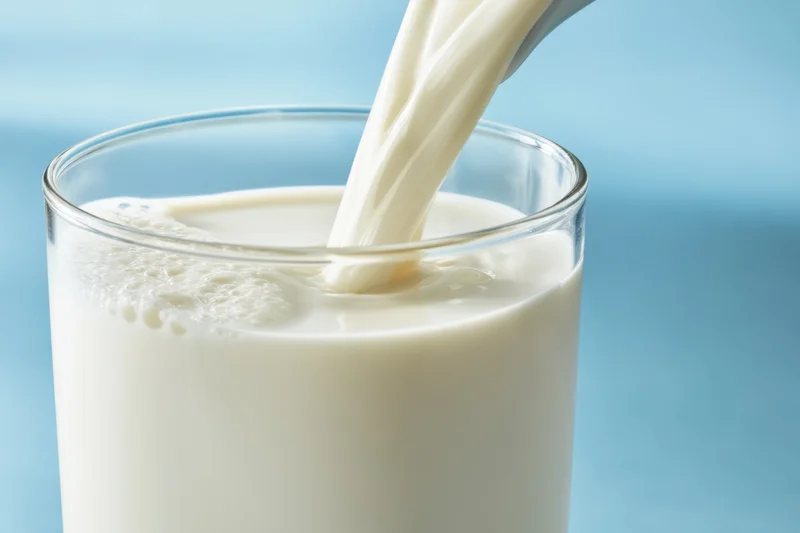 Milk being poured into a glass from above against a blue background